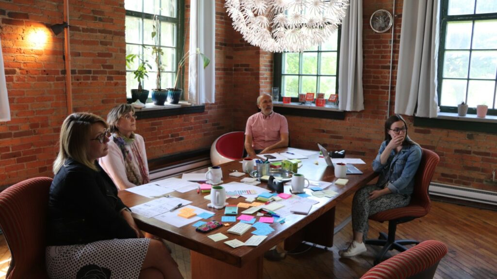 Coaching de groupe : quatre femmes autour d'une table couverte de post-its, dans une salle aux murs de brique