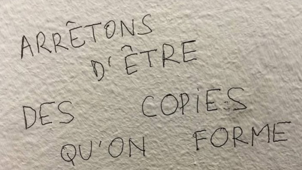Inscription manuscrite au mur : « Arrêtons d'être des copies qu'on forme »