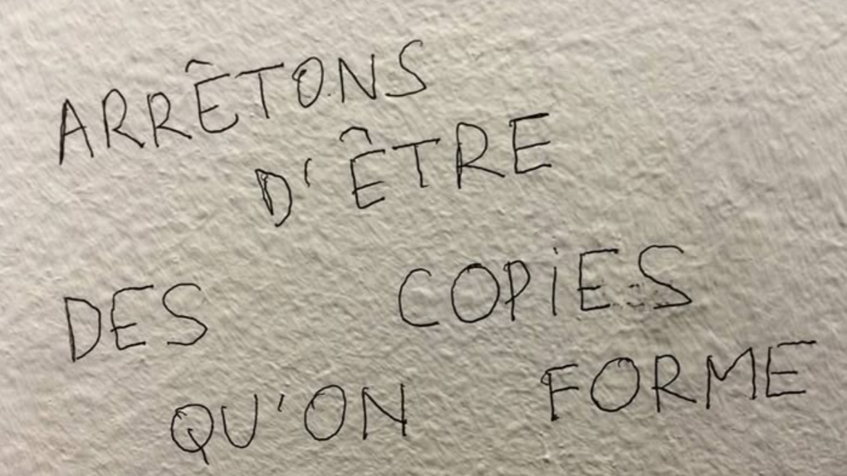 Inscription manuscrite au mur : « Arrêtons d'être des copies qu'on forme »